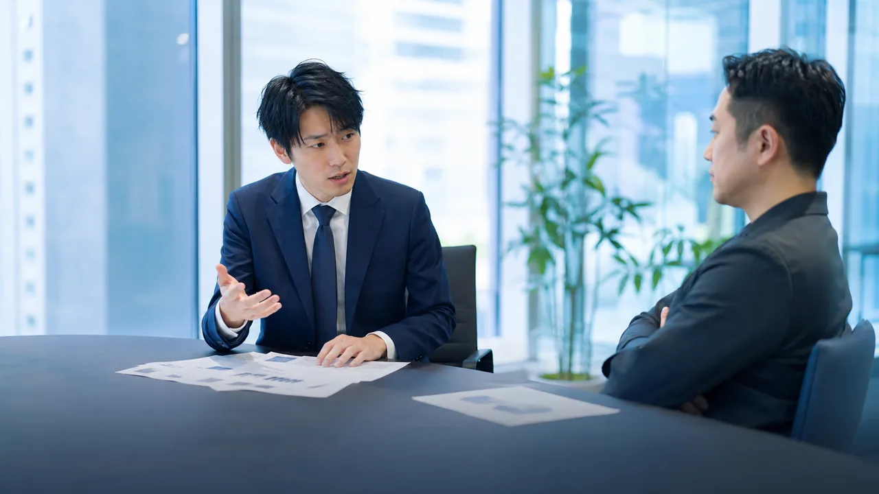 手元の資料を確認しながら顧客に説明する営業担当者